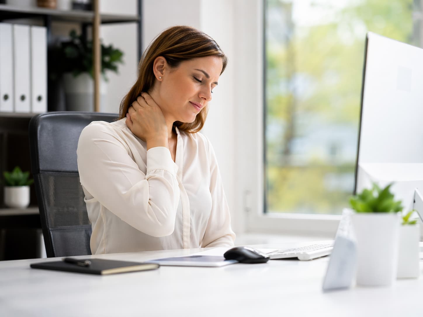 Office worker at her desk with one hand on her neck, showing mild discomfort from prolonged desk work